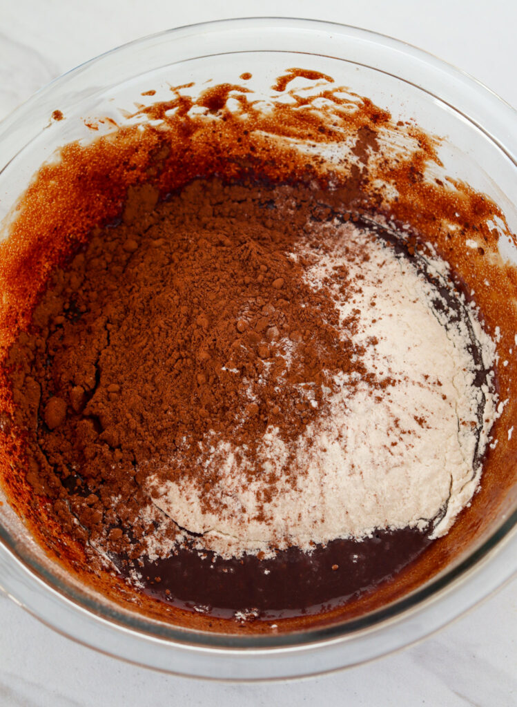 A bowl full of flour and coco powder is added to the chocolate mixture