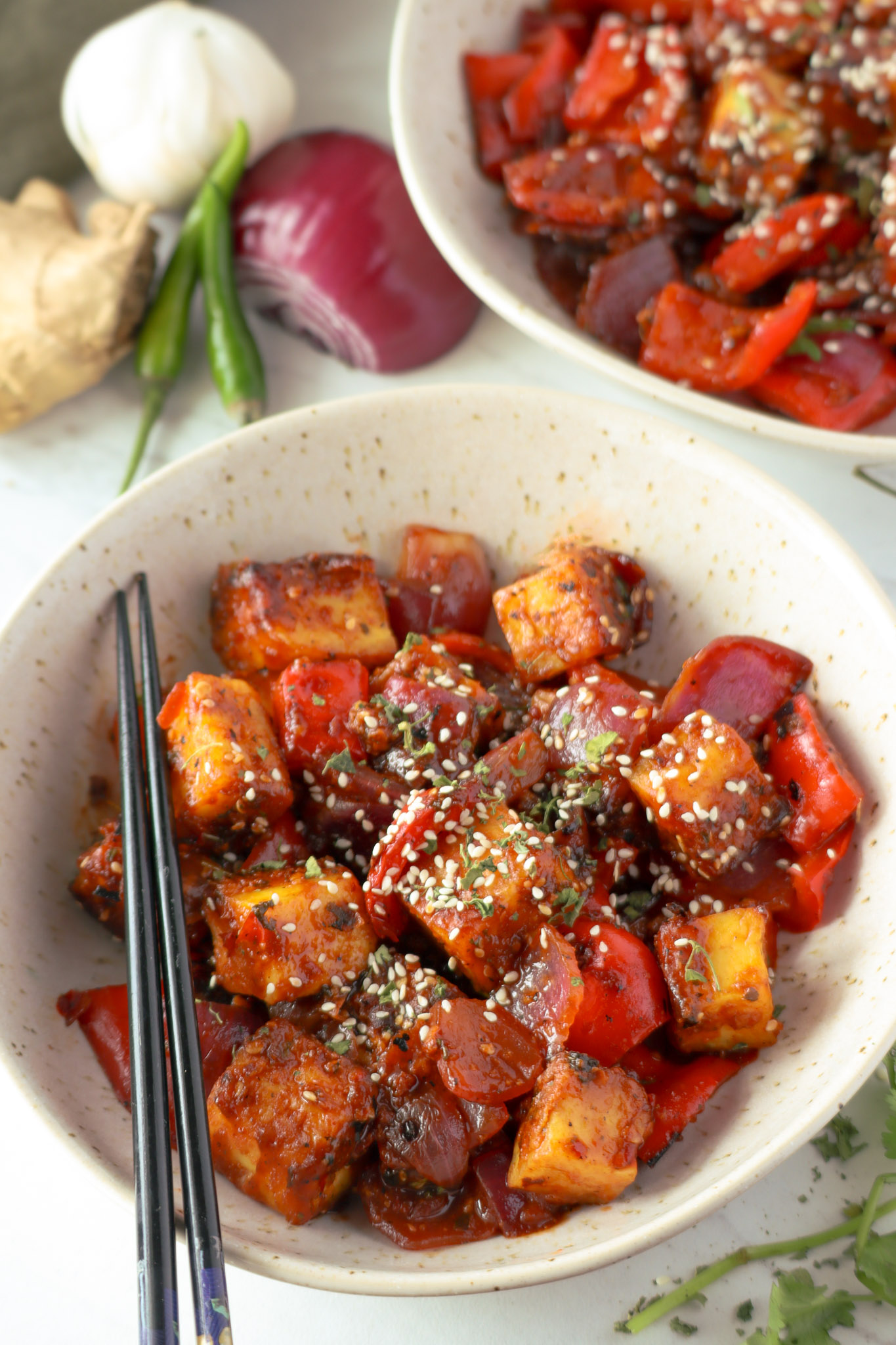 two bowls of chili paneer, topped with sesame seeds for garnish